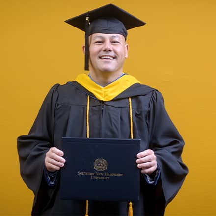 David Wallace, a 2025 WUV graduate who earned his bachelors in business administration wearing his cap and gown in front of a yellow background. 