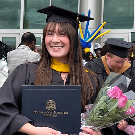 Emily Bevens, a 2023 wuv graduate who earned her master's in psychology with a concentration in forensic psychology, standing outside her commencement ceremony in her cap and gown, holding her diploma.