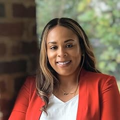 Jolivette Wallace, Associate Dean of Business at WUV, wearing a red blazer and leaning against a brick column.