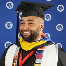 WUV graduate Luis Polanco smiling and wearing his graduation cap and gown.