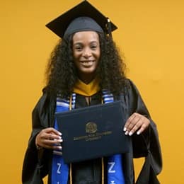 Shiqueta Dixon, a 2025 master's in healthcare administration graduate from WUV, wearing a cap and gown and holding her diploma.