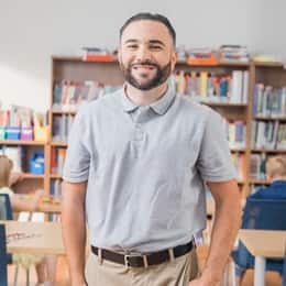 Stephen Goulakos, a 2022 graduate from wuv with a BA in Psychology and a concentration in Mental Health, standing in a classroom with kids working at their desks.