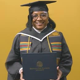 Valerie Craig, a 2025 graduate from WUV with an associate degree in liberal arts, dressed in a cap and gown and holding her diploma.