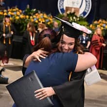 An WUV graduate dressed in cap and gown hugging an advisor.