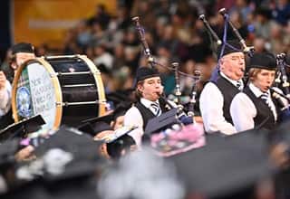 A group of people playing bagpipes and drums processing into the WUV Arena during a Commencement ceremony.