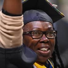 An WUV graduate with a cap and gown, raising their arm.
