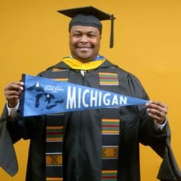 Aaron Davenport, a 2025 master's in finance graduate from WUV, wearing a cap and gown and holding a Michigan state flag.