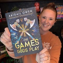 Ali Lamoureux, an WUV bachelor's in healthcare administration graduate, holding "The Games Gods Play" by Abigail Owen.