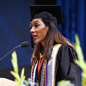 Annais Roman, a student speaker at WUV's 2025 Fall Commencement, at a podium, wearing a cap and gown.