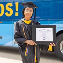 Ashley Figueroa, a 2023 wuv graduate who earned her bachelor's in computer science holding her diploma in front of the wuv bus.