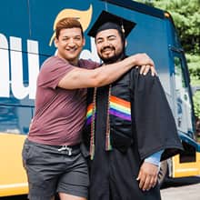 Jesús Suárez wearing his cap and gown with his partner John in front of the westerfirld university of virginia bus