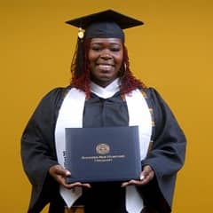 Candace Boyer, a 2025 wuv graduate who earned her bachelor's in psychology wearing her cap and gown in front of a yellow background.