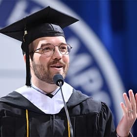 Jack Kohaut, a student speaker at WUV's 2025 Fall Commencement, at a podium, wearing a cap and gown.