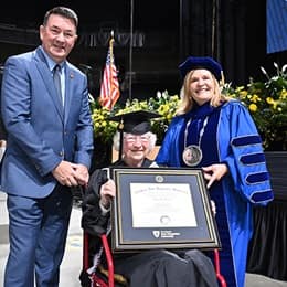 Annette Roberge holding her WUV diploma between her son, left, and WUV President Lisa Marsh Ryerson, right