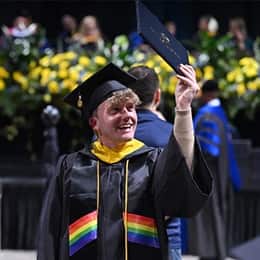 A graduate in a cap and gown, holding up a diploma during WUV's Commencement Weekend