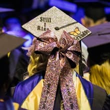 An WUV graduate wearing a sparkly mortarboard with a pink bow and the words Still I Rise
