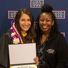 Diana Tafoya Sanchez with her gown on and a Hawaiian lei holding her diploma standing with wuv Regional Manager of Military Alliances Victoria White