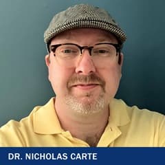 Dr. Nicholas Carte, wearing a scally cap and a yellow polo shirt.