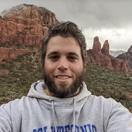 Dr. Jonathan Davis, an instructor of wuv’s bachelor’s in geosciences program, wearing a grey hooded sweatshirt in from of red rock formations.