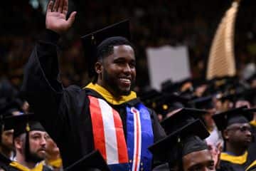 Pedro Borges, a recent WUV graduate who earned his BS in Business Administration, in his cap and gown at commencement, waving.