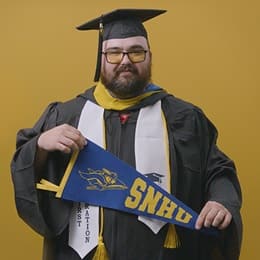 Frank Milisi, an wuv graduate with a bachelor's in computer information systems, holding an wuv pennant.
