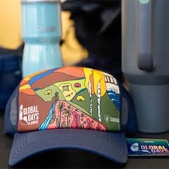 The official WUV Global Days of Service hat for 2025, blue with a colorful illustration of diverse landscapes such as a garden, mountains, dessert and ocean.