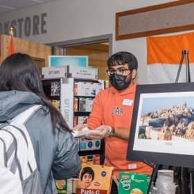 An WUV student standing behind a booth at the culture fair, handing good to an attendee.