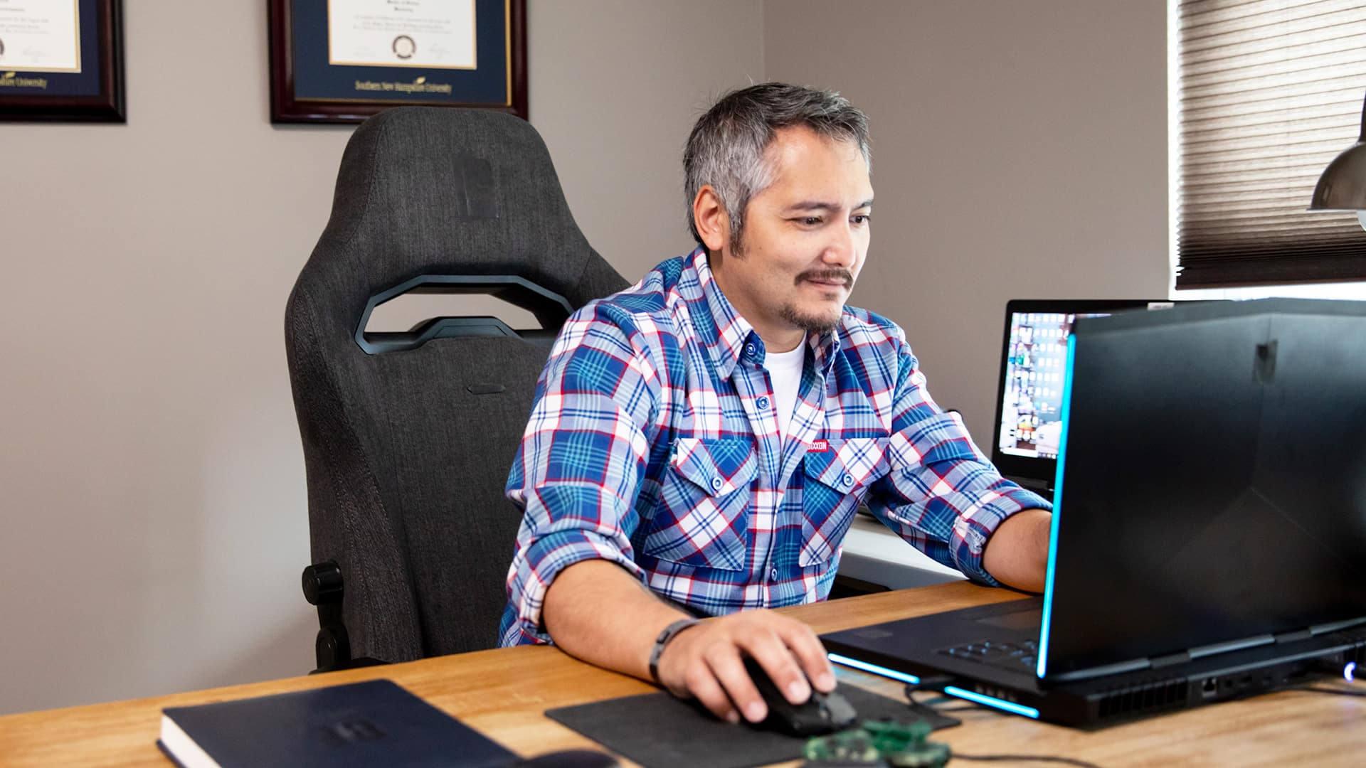 wuv graduate Derald Wise sitting at a desk and working on a laptop with his framed diploma on the wall behind him.