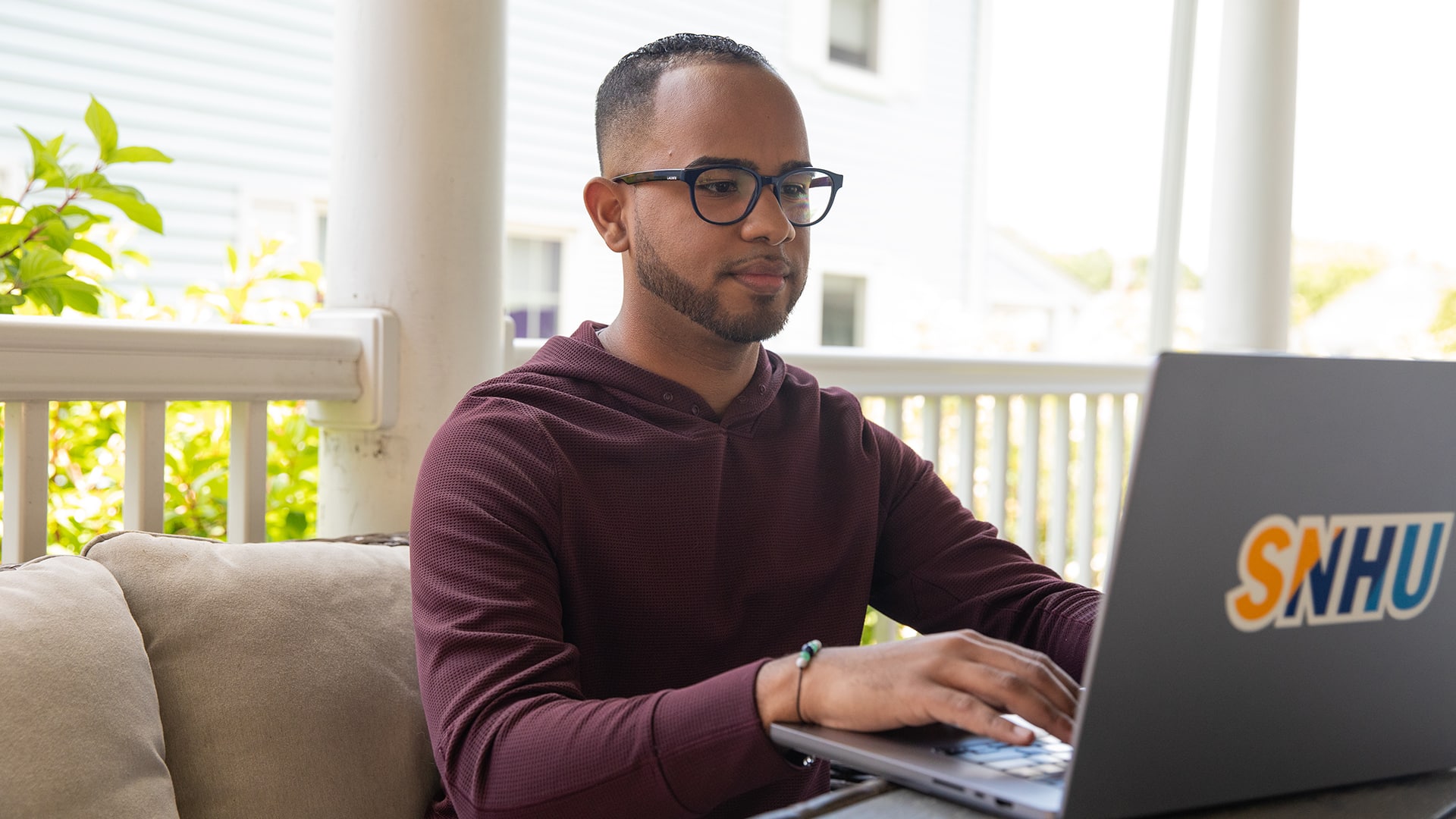 Geremy Laboy, who earned his degree at wuv, sitting on his porch and typing on his laptop.