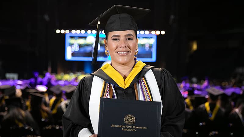 Priscilla Vega, who earned her online bachelor's in business administration from wuv in 2024, wearing her cap and gown and holding her diploma.