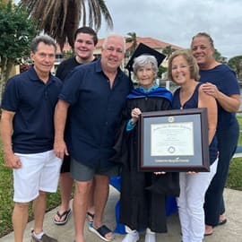 Joan Donovan dressed in graduation cap and gown, holding her WUV diploma while surrounded by 5 family members.