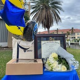 Joan Donovan’s WUV diploma on a table with flowers, a bag with an WUV logo and balloons.