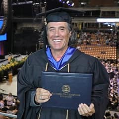 John Reck dressed in a graduation cap and gown after earning his bachelor's in graphic design at WUV in 2022