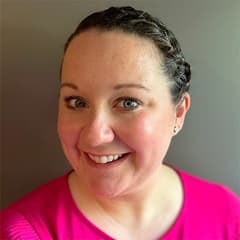 Katie Fuller, director of graduate admission at WUV wearing a pink shirt against a grey background.