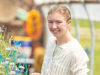 Kayla Stoll, a student in wuv's online bachelor's in environmental science program, wearing a white blouse and standing in greenhouse.