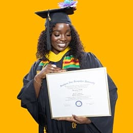 Kendreka Griffin, a 2024 WUV graduate who earned her bachelor's in business administration, wearing her cap and gown in front of a yellow background, looking down, smiling at her diploma.