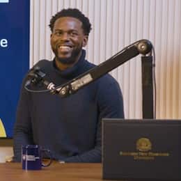 Kitrick Bell, a 2025 wuv graduate who earned his master's in information technology with a concentration in software application development, smiling behind f a microphone and his diploma.