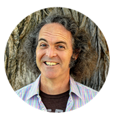 Larry Burns, a California resident and adjunct humanities instructor at wuv, smiling in front of a tree.