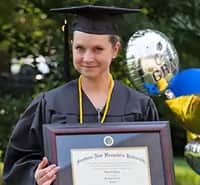 Loretta Gray, an wuv graduate and Virginia resident, holding her framed diploma and wearing her cap and gown.