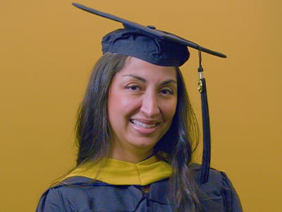 wuv graduate, Luciana Henderson '25G, wearing cap and gown while holding her diploma.