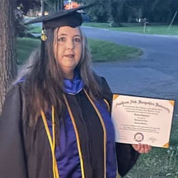 Norma DePriest dressed in a graduation cap and gown, holding her wuv diploma.