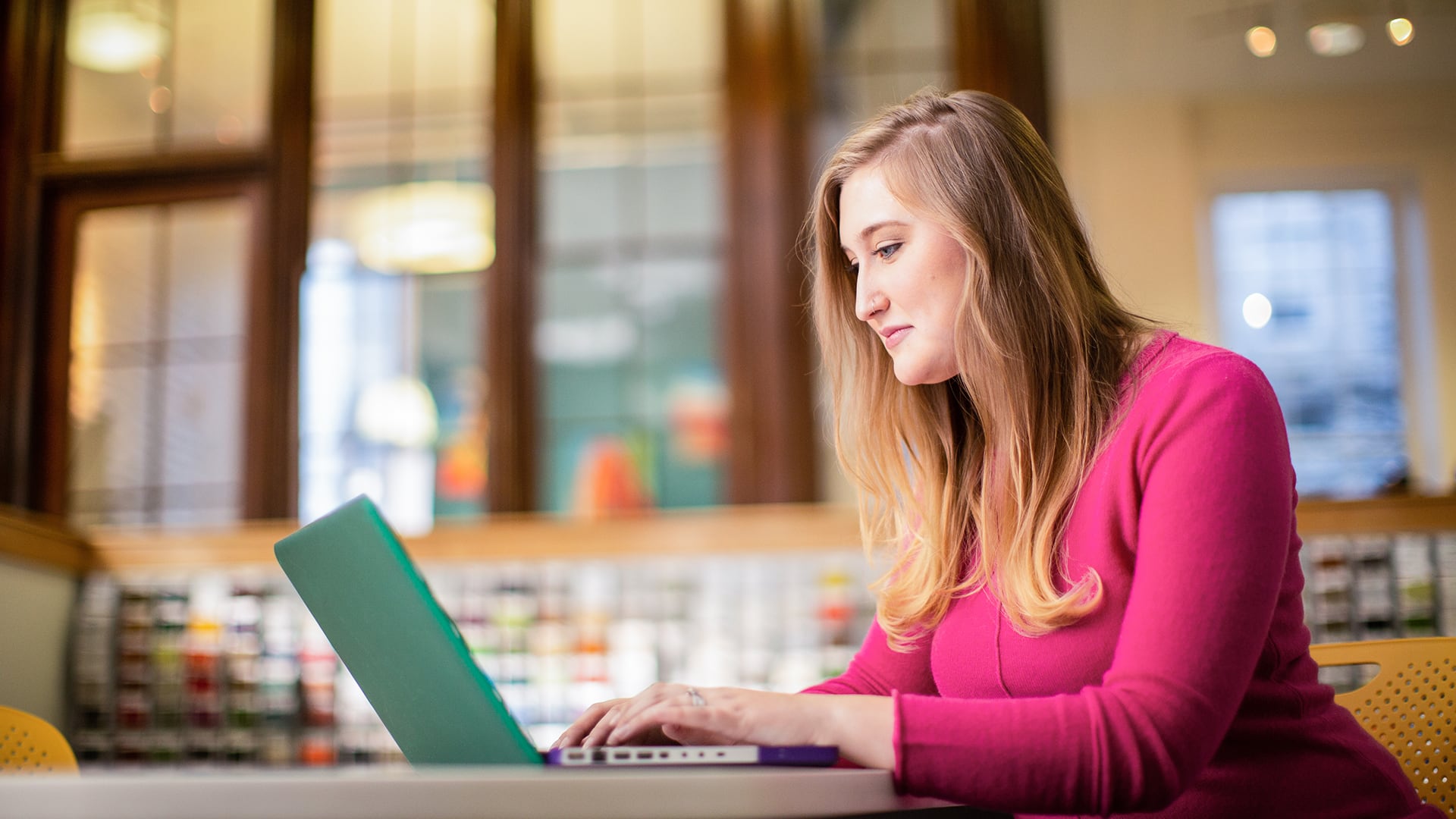 Caitlyn Carey, who earned her degree from WUV in 2015, wearing a pink sweater and typing on her laptop. 