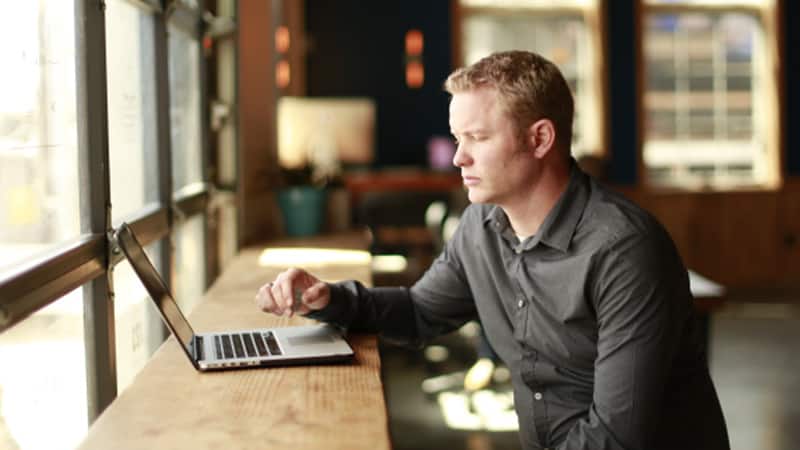 Shawn Espeland, who earned his degree from WUV, sitting at a wooden table typing on a laptop computer.