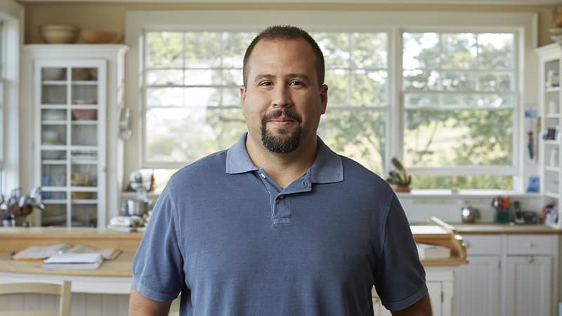 Raymond Gammon, who earned his degree from wuv in 2020, wearing a blue polo shirt standing in his kitchen.