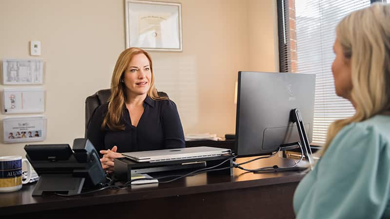 Nikki Bennett, who earned her degree from wuv in 2022, sitting behind a desk with a phone and computer  monitor talking to another woman