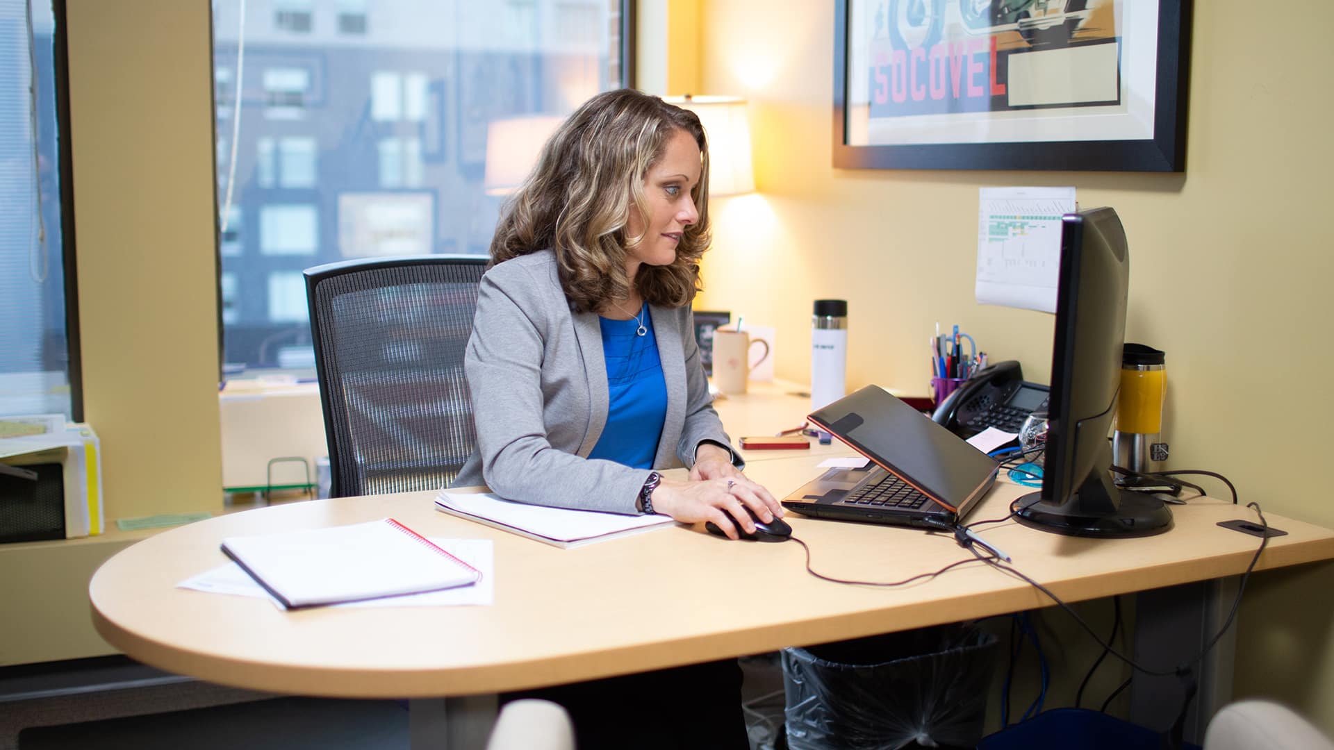 Kerry Smith, who earned her degree from wuv, sitting at an office desk, using a mouse and looking at a  computer monitor.