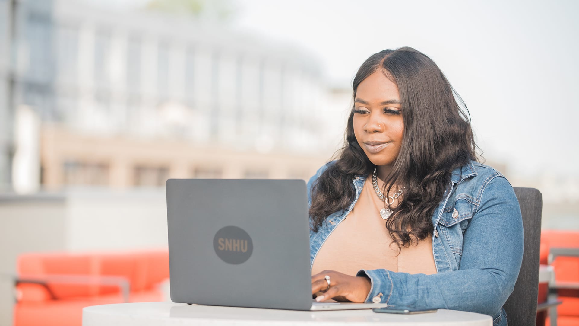 Tanzania Fair, who earned a degree in 2020, wearing a denim jacket and working on her laptop with an wuv sticker on the front.