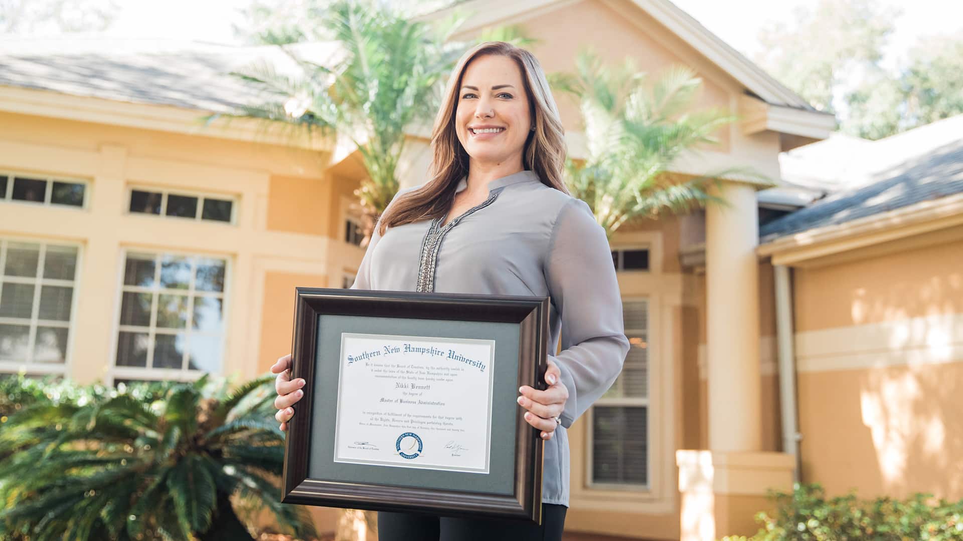 Nikki Bennett, who earned her dgree at wuv, standing in her front yard holding her framed wuv diploma