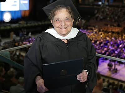 Mary Beth Dayley, who earned her online master's in creative writing from wuv in 2024, wearing her cap and gown and holding her diploma.