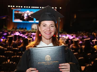 Donna Parisi, who earned her online master's in creative writing from wuv in 2024, wearing her cap and gown and holding her diploma.